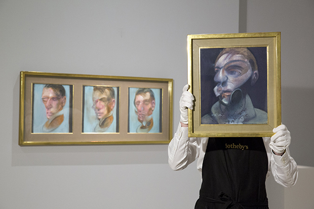 A Sotheby's employee holding Francis Bacon, Self-Portrait, 1975,  oil on canvas, 35.5 by 30.5cm, est. £10-15 million. Behind: Francis Bacon, Three Studies for Self-Portrait, 1980, oil on canvas, each: 35.5 by 30.5cm est. £10-15 million. Courtesy of Sotheby’s