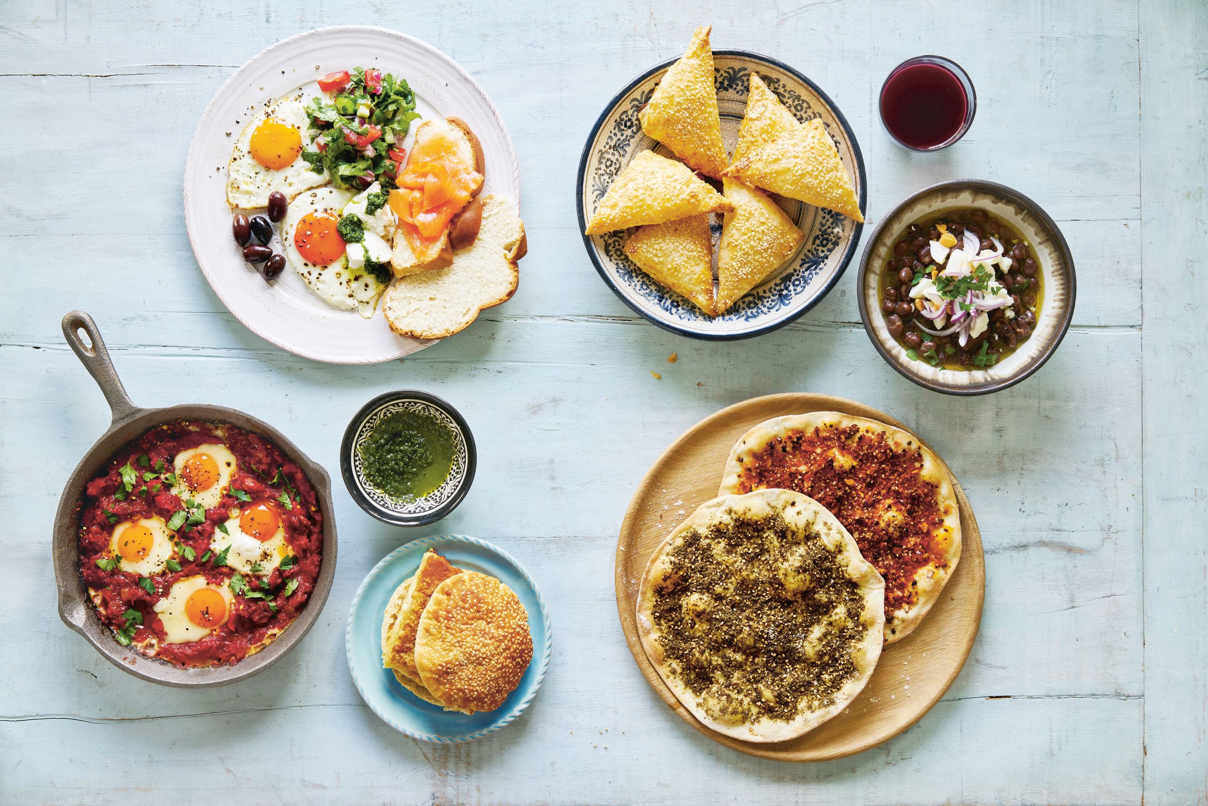 Clockwise from top left: Israeli breakfast plate; cheese-stuffed puff pastry; pomegranate juice; Egyptian fava bean stew; flatbreads with za'atar and keshek; knafeh sandwich with kataifi crust; Israeli shakshuka, as reproduced in Breakfast: The Cookbook